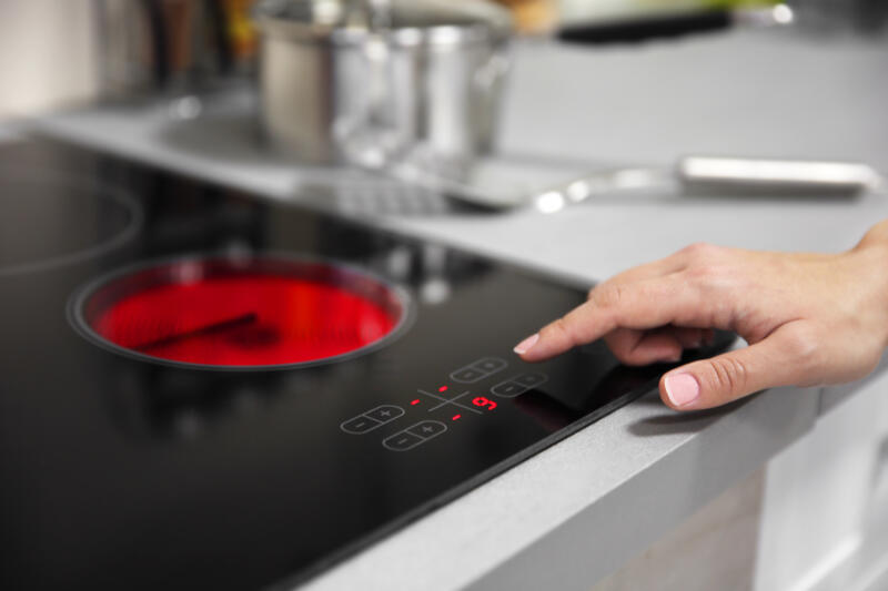Female hand turns on electric hob closeup